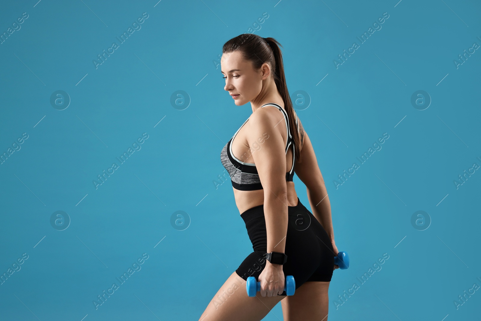 Photo of Woman in gym clothes exercising with dumbbells on light blue background