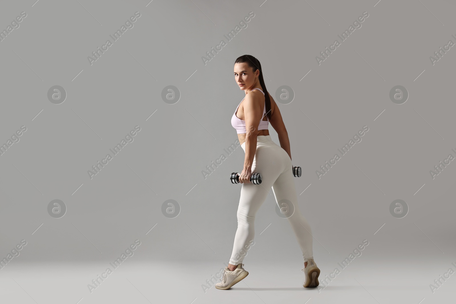 Photo of Woman in gym clothes exercising with dumbbells on grey background, space for text