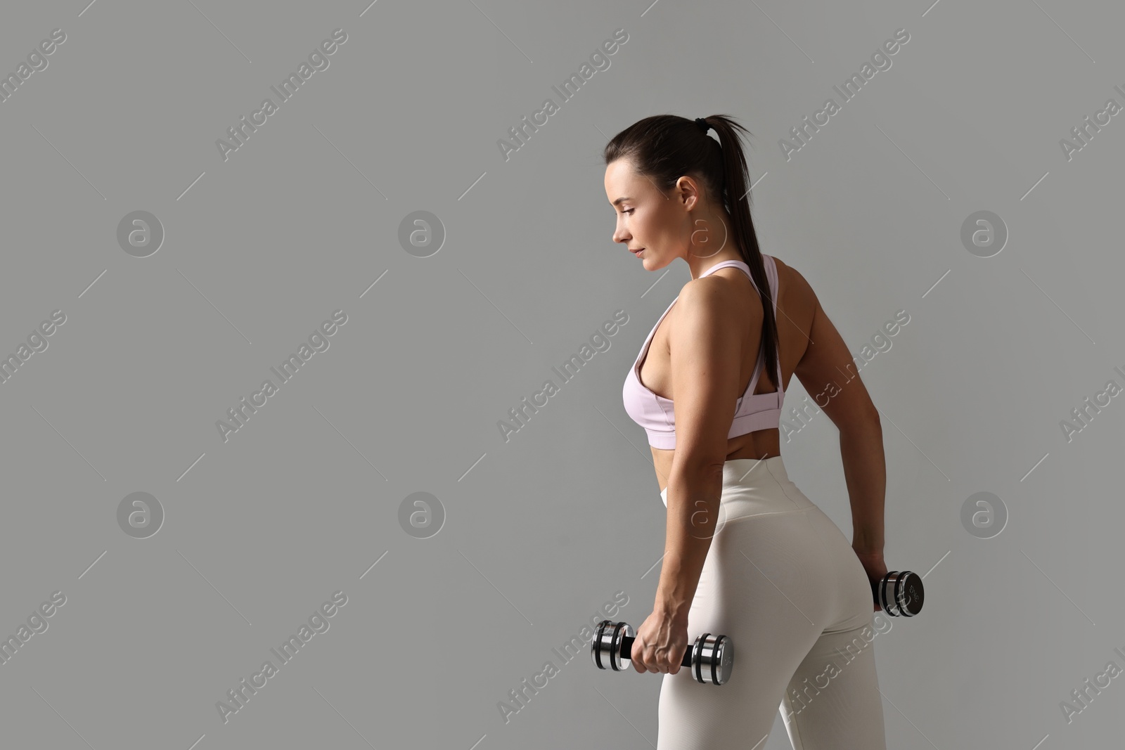 Photo of Woman in gym clothes exercising with dumbbells on grey background, space for text