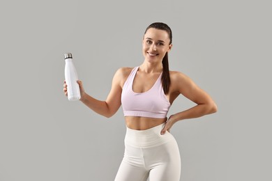 Photo of Woman in gym clothes with thermo bottle on grey background