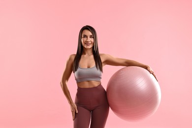 Photo of Woman in gym clothes with fitness ball on pink background