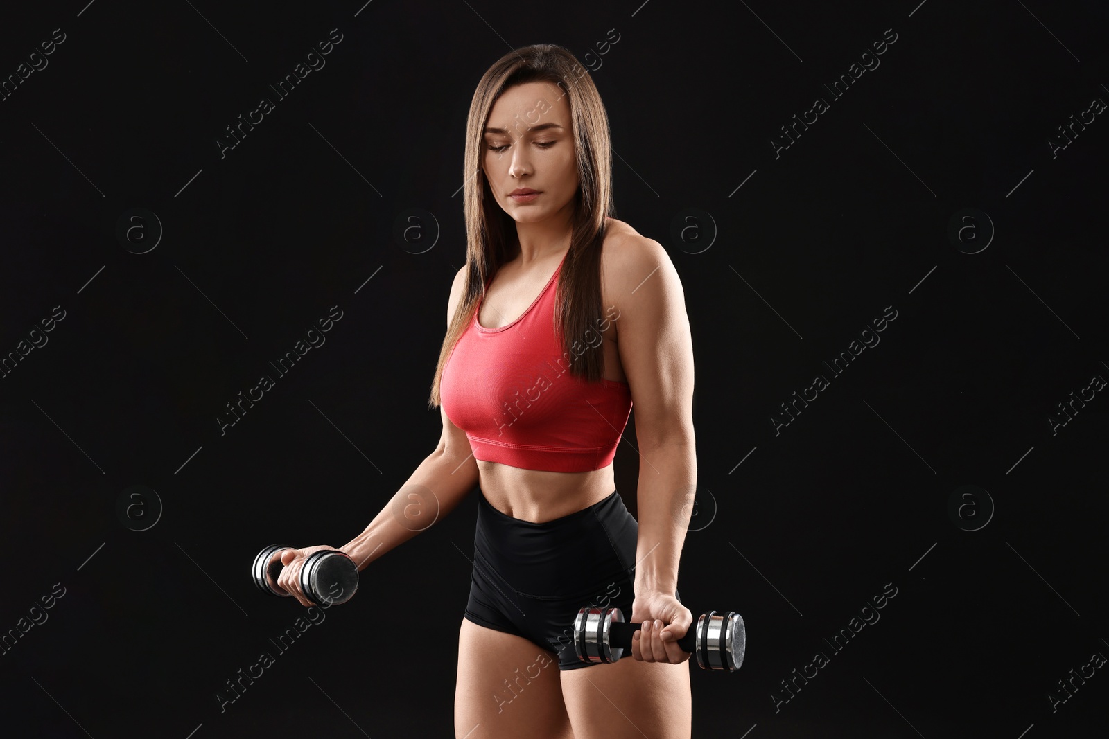 Photo of Woman in gym clothes exercising with dumbbells on black background