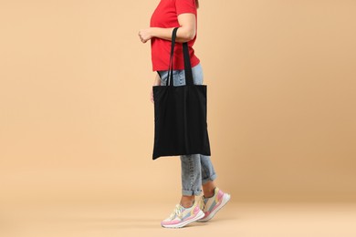 Photo of Woman with blank black shopper bag on color background, closeup. Mockup for design