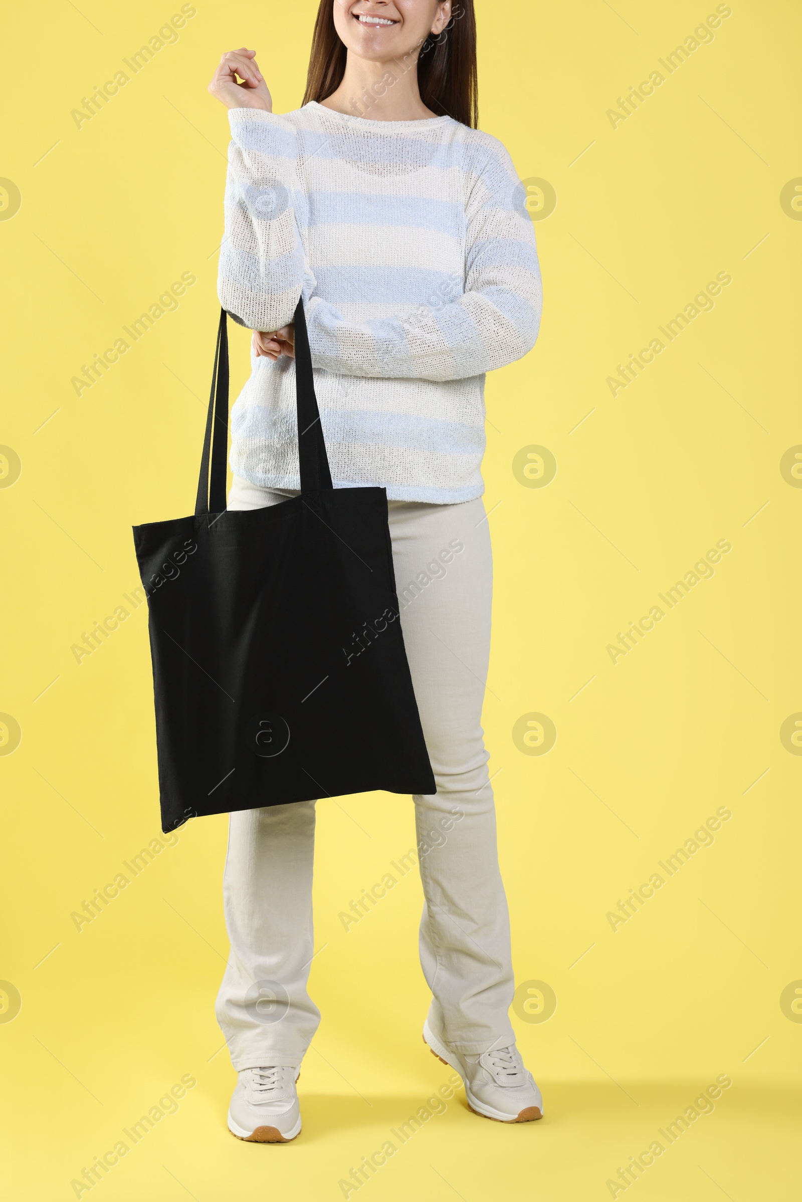 Photo of Woman with blank black shopper bag on yellow background, closeup. Mockup for design