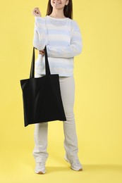 Photo of Woman with blank black shopper bag on yellow background, closeup. Mockup for design