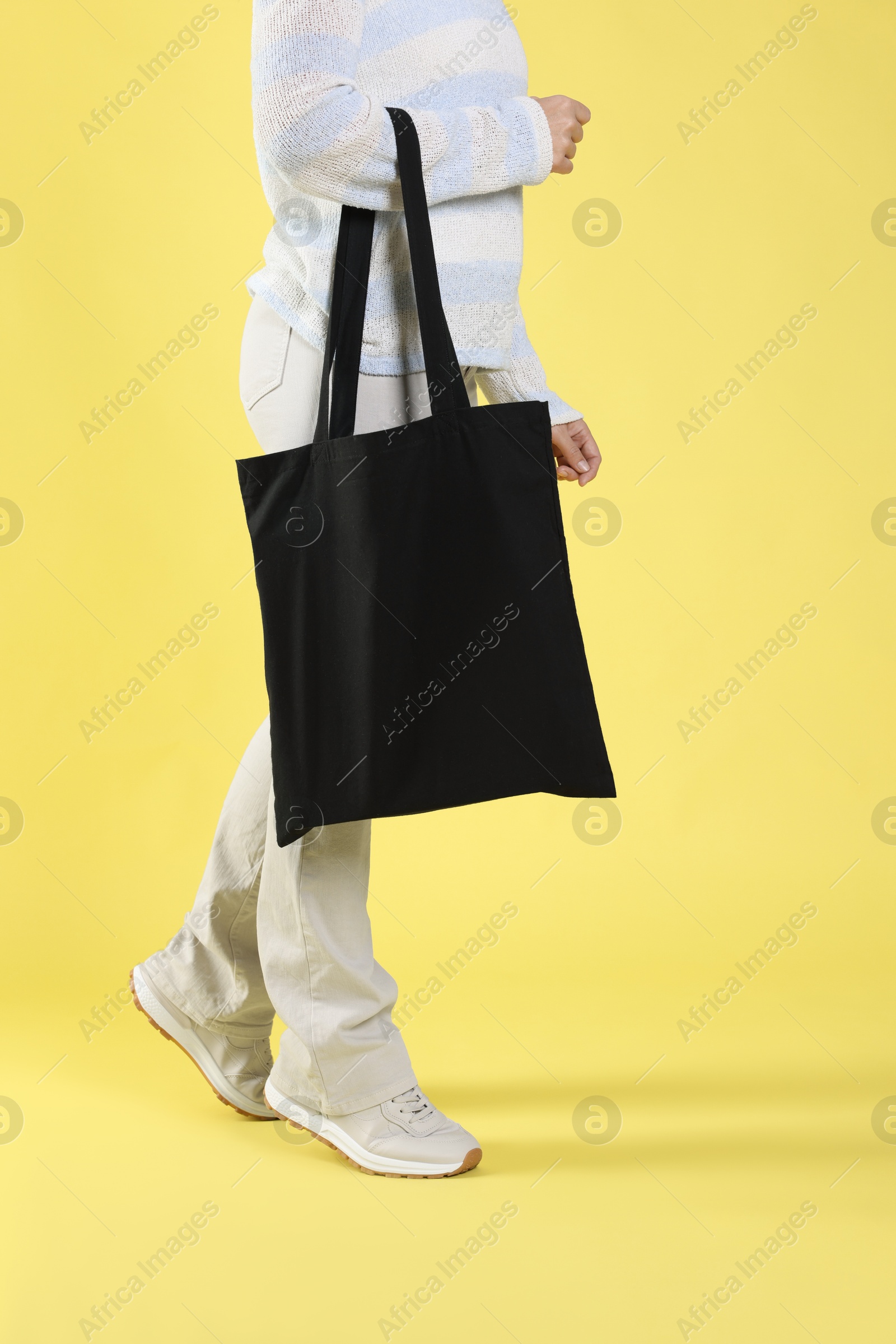 Photo of Woman with blank black shopper bag on yellow background, closeup. Mockup for design