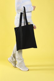 Photo of Woman with blank black shopper bag on yellow background, closeup. Mockup for design