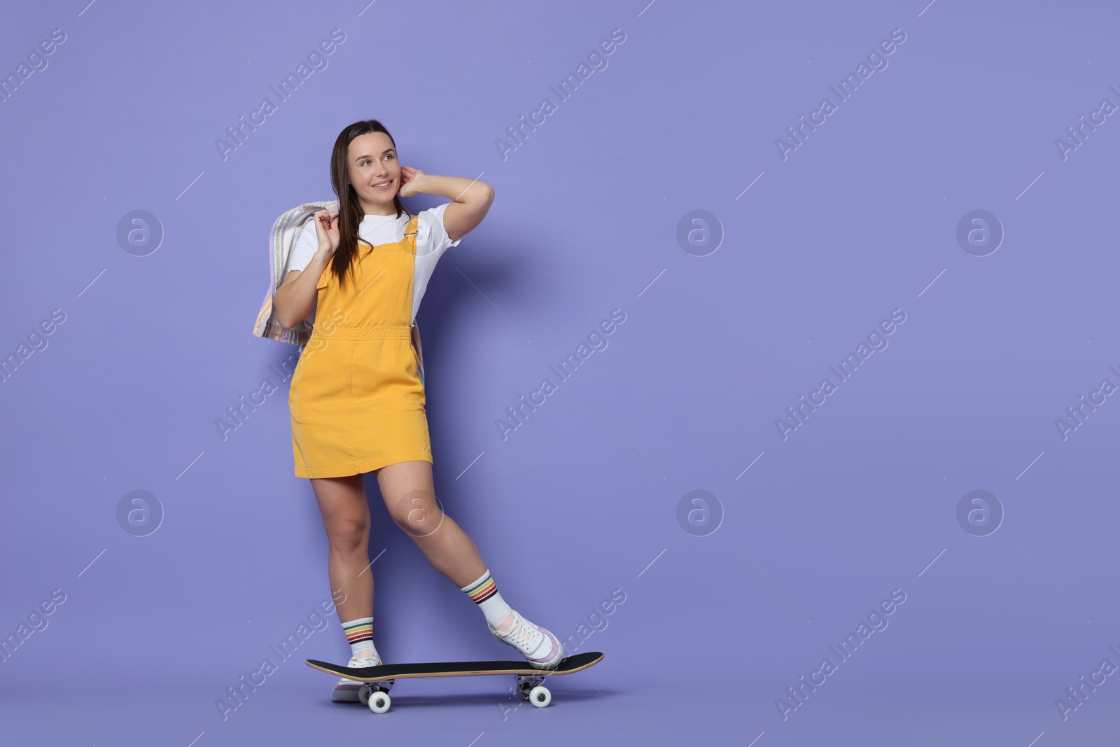 Photo of Smiling woman with skateboard on violet background. Space for text