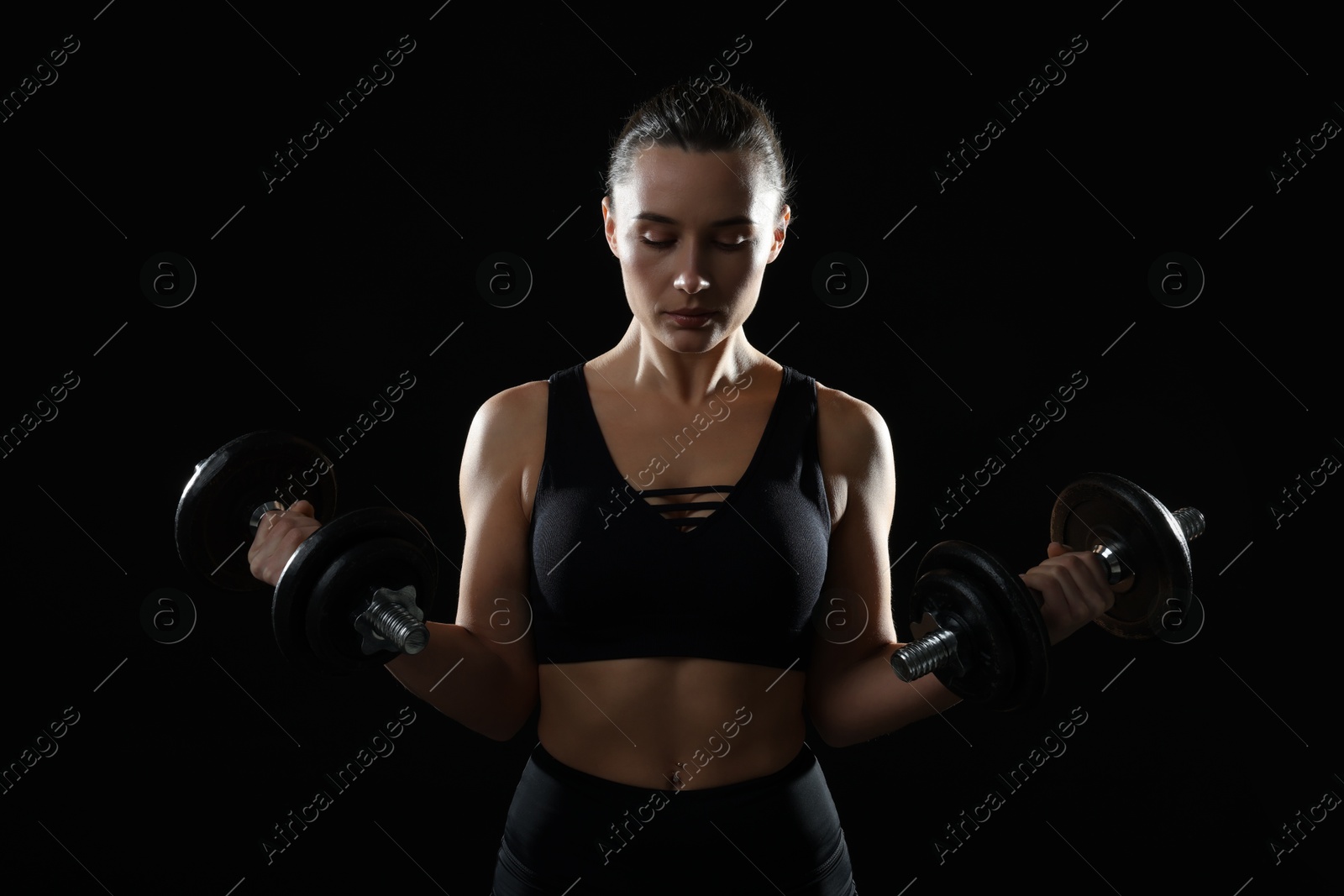 Photo of Beautiful woman in sportswear training with barbells on black background