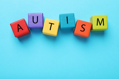 Photo of Word Autism made of colorful cubes on light blue background, top view. Space for text