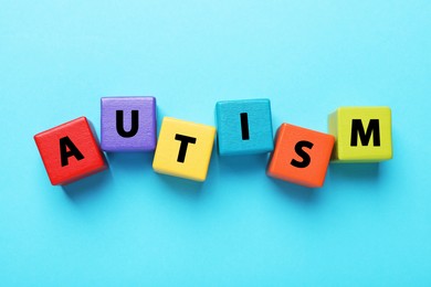 Photo of Word Autism made of colorful cubes on light blue background, top view