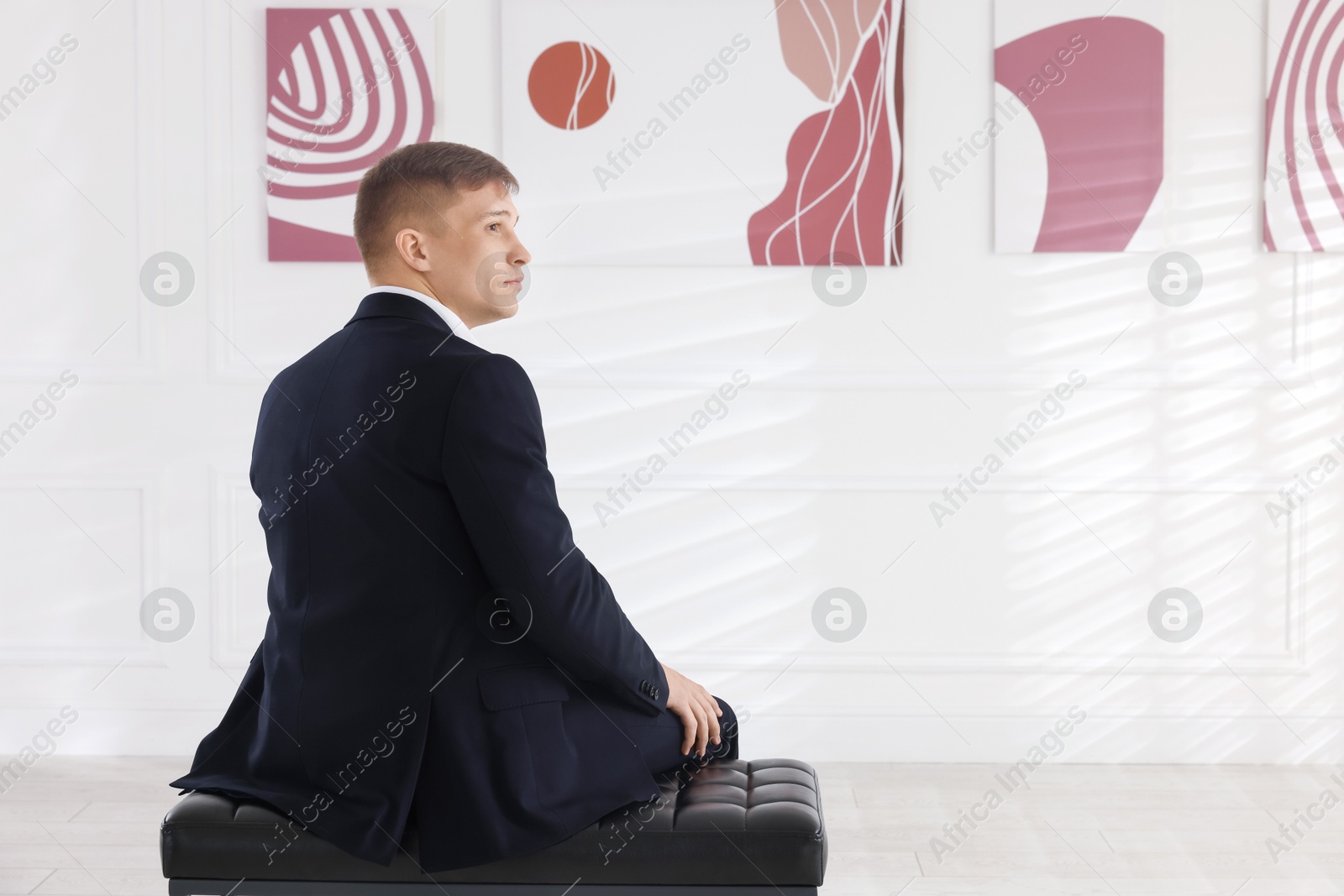 Photo of Man sitting on bench and looking at paintings in art gallery