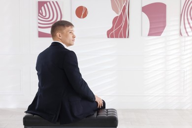 Photo of Man sitting on bench and looking at paintings in art gallery