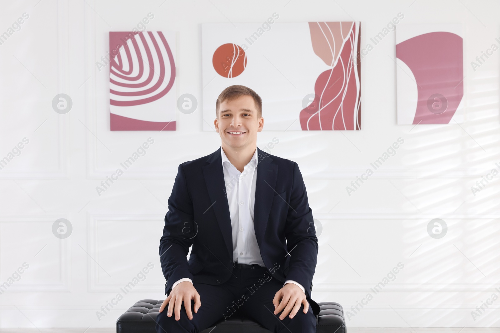 Photo of Man sitting on bench and looking at paintings in art gallery