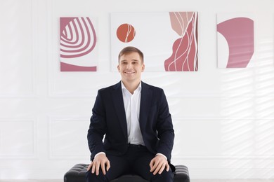 Photo of Man sitting on bench and looking at paintings in art gallery