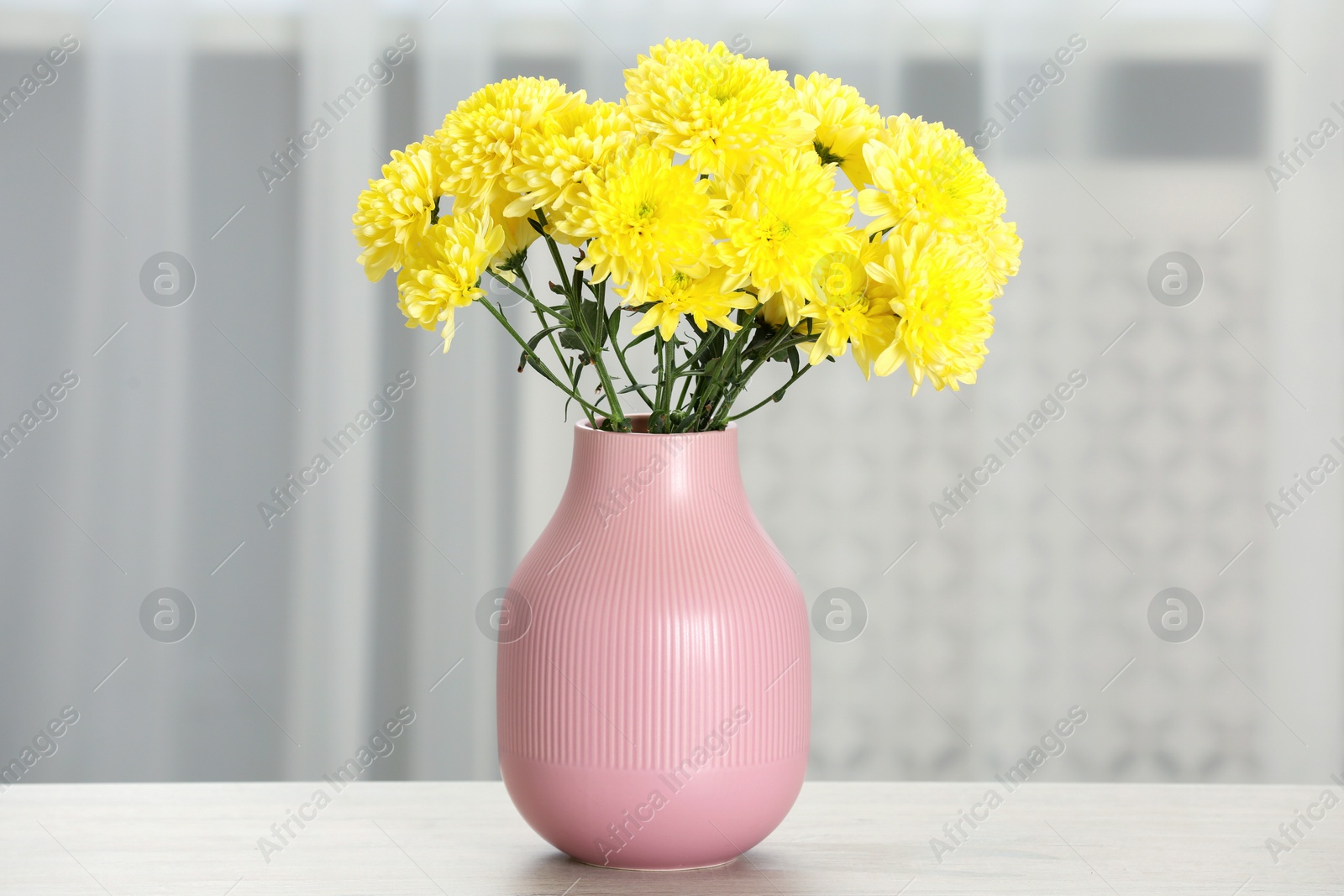 Photo of Beautiful yellow flowers in vase on table at home