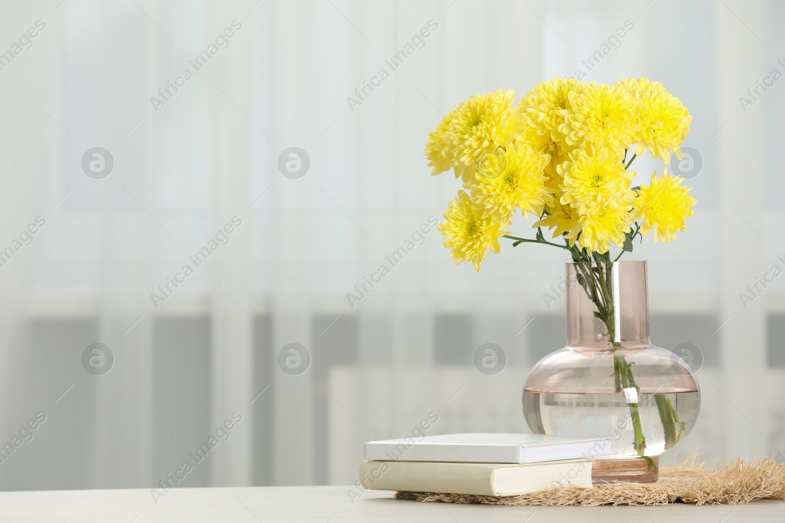 Photo of Beautiful yellow flowers in vase and books on table at home, space for text