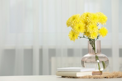 Photo of Beautiful yellow flowers in vase and books on table at home, space for text