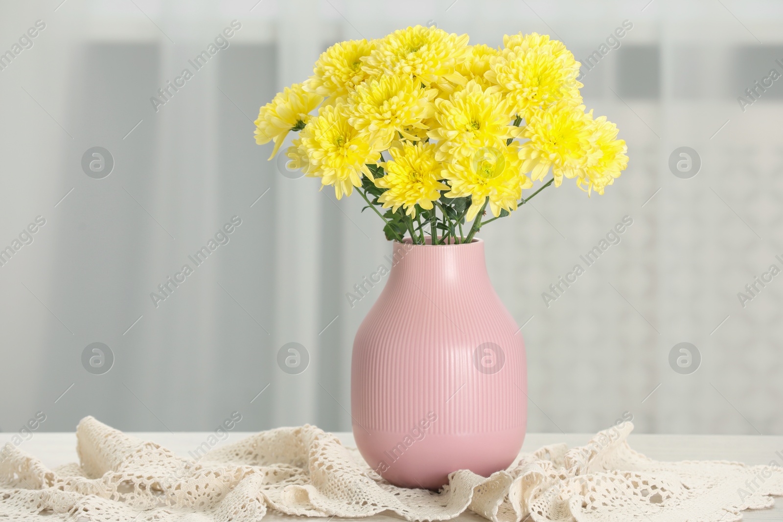 Photo of Beautiful yellow flowers in vase on table at home