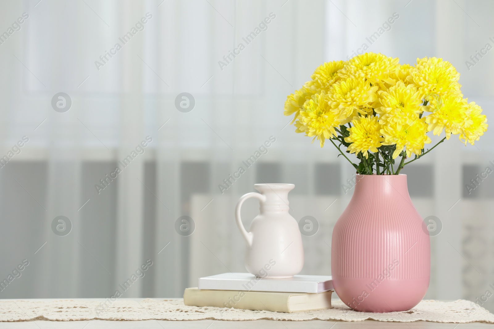 Photo of Beautiful yellow flowers in vase and books on table at home, space for text