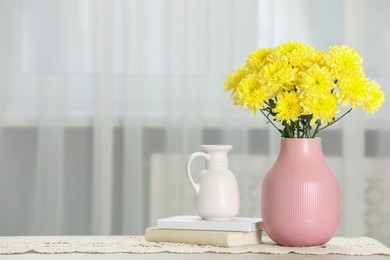 Photo of Beautiful yellow flowers in vase and books on table at home, space for text