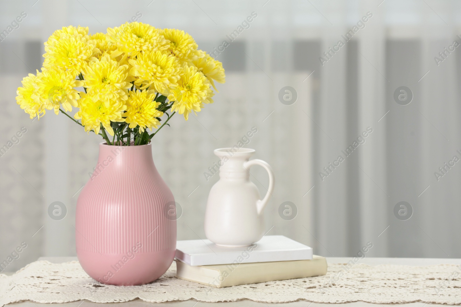 Photo of Beautiful yellow flowers in vase and books on table at home, space for text