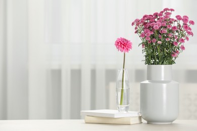 Photo of Beautiful pink flowers in vases and books on table at home, space for text