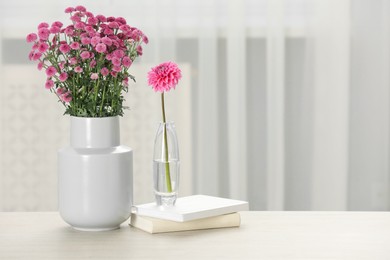 Photo of Beautiful pink flowers in vases and books on table at home, space for text