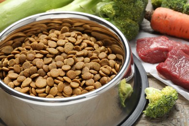 Photo of Dry pet food in feeding bowl among natural products on wooden table, closeup