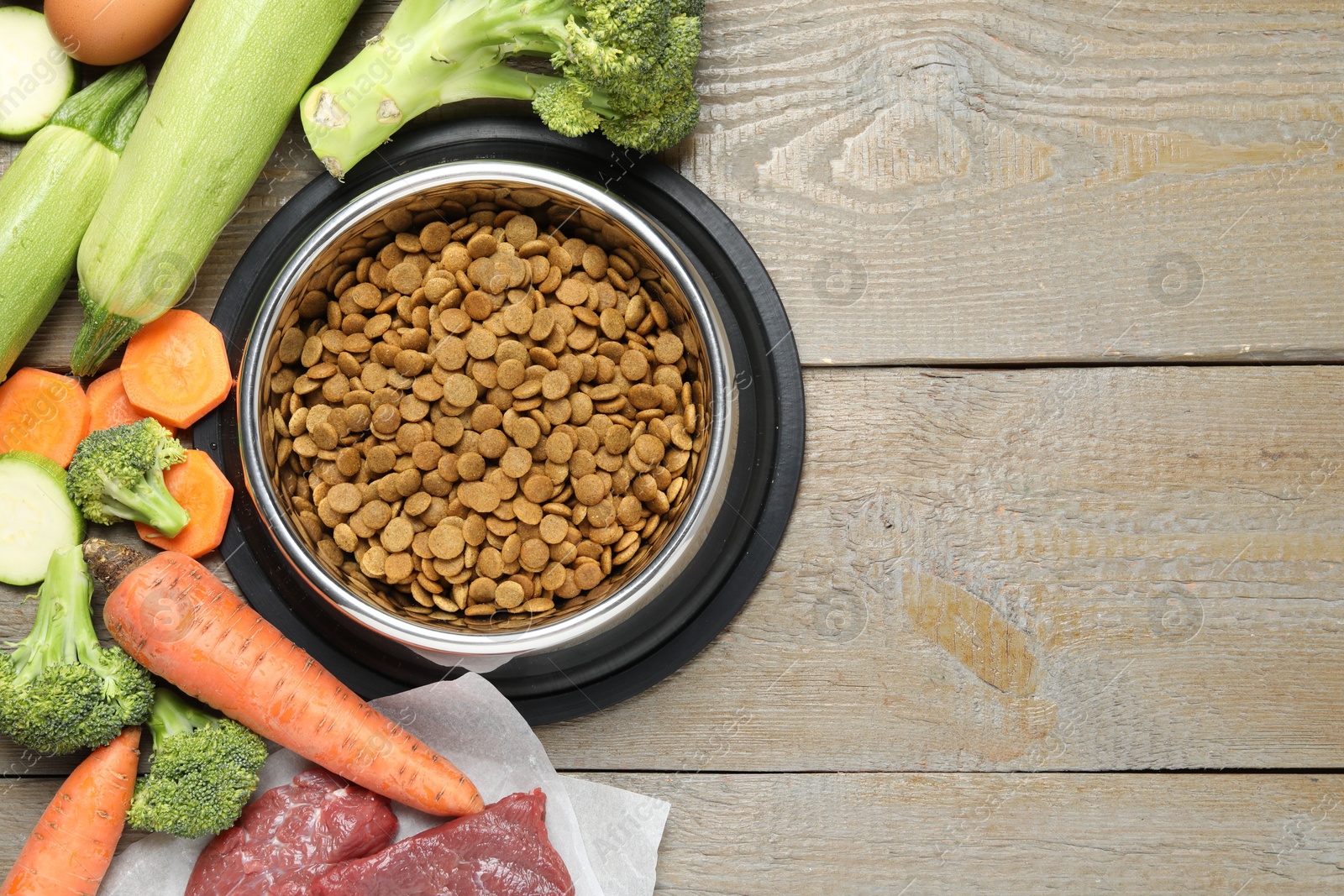 Photo of Dry pet food in feeding bowl and natural products on wooden table, flat lay. Space for text