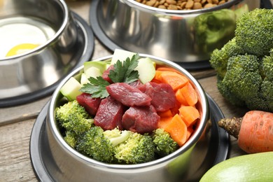 Photo of Fresh natural pet food in feeding bowl and vegetables on wooden table, closeup