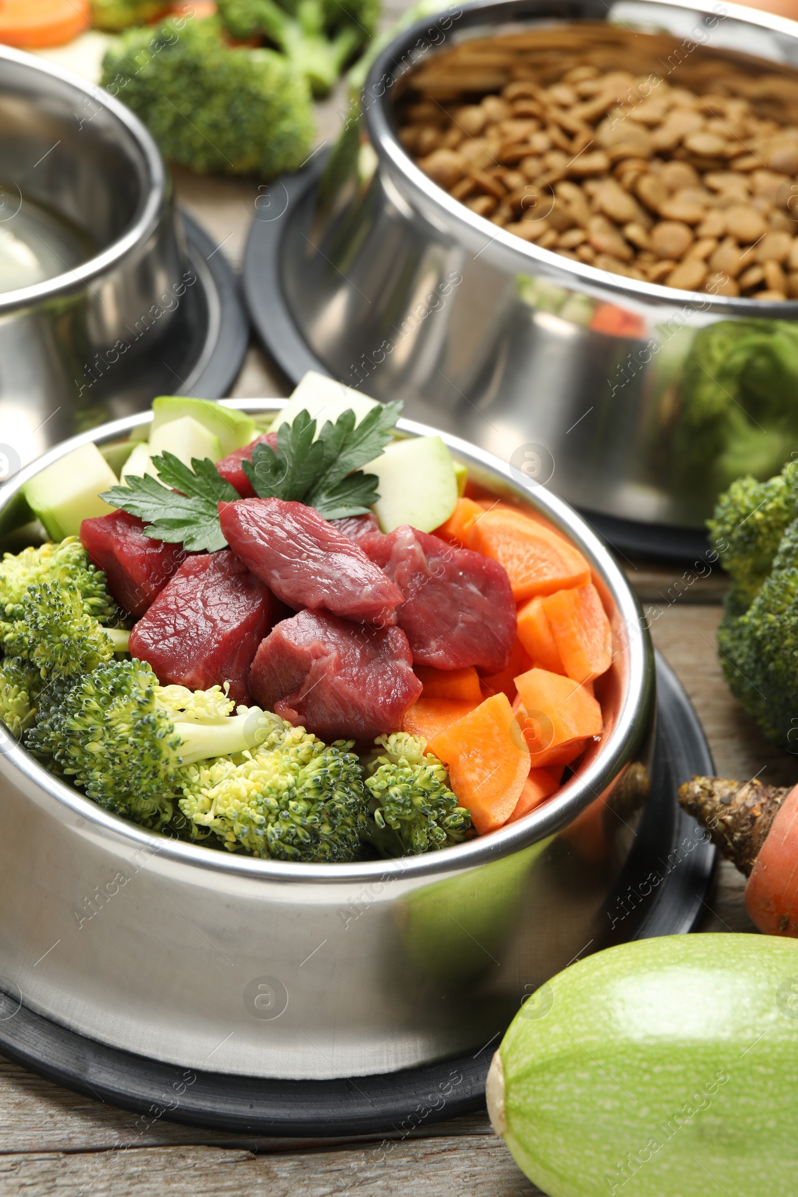 Photo of Fresh natural pet food in feeding bowl and vegetables on wooden table, closeup