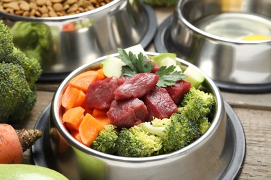 Photo of Fresh natural pet food in feeding bowl and vegetables on wooden table, closeup