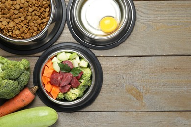 Photo of Dry and natural pet food in feeding bowls on wooden table, flat lay. Space for text