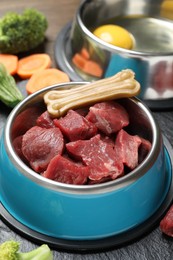 Photo of Pet food. Fresh beef in feeding bowl and chew bone on dark textured table, closeup