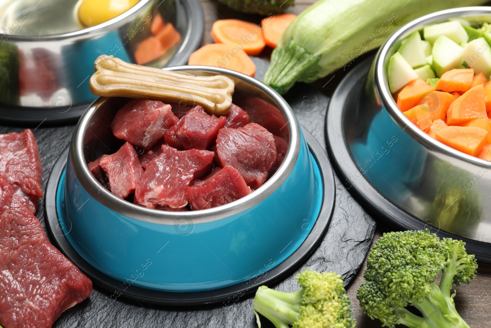 Photo of Pet food. Fresh beef in feeding bowl and chew bone among products on table, closeup