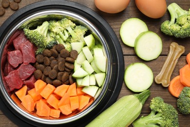 Photo of Dry and natural pet food in feeding bowl among products on wooden table, flat lay