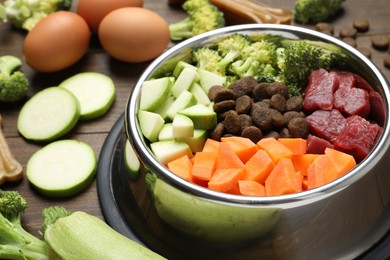 Photo of Dry and natural pet food in feeding bowl among products on wooden table, closeup