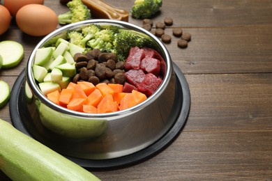 Photo of Dry and natural pet food in feeding bowl among products on wooden table, closeup. Space for text