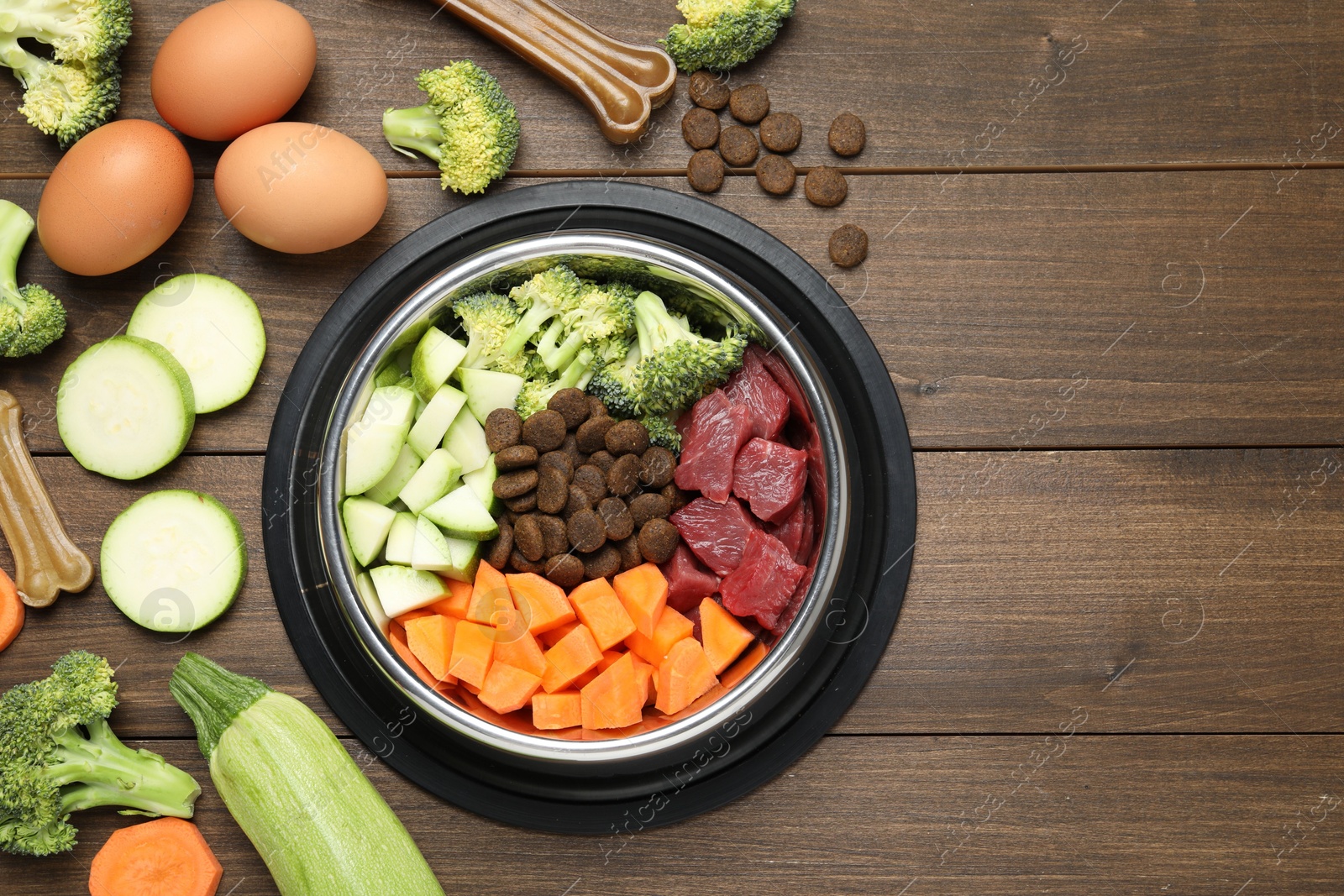 Photo of Dry and natural pet food in feeding bowl among products on wooden table, flat lay. Space for text