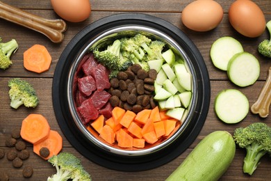 Photo of Dry and natural pet food in feeding bowl among products on wooden table, flat lay