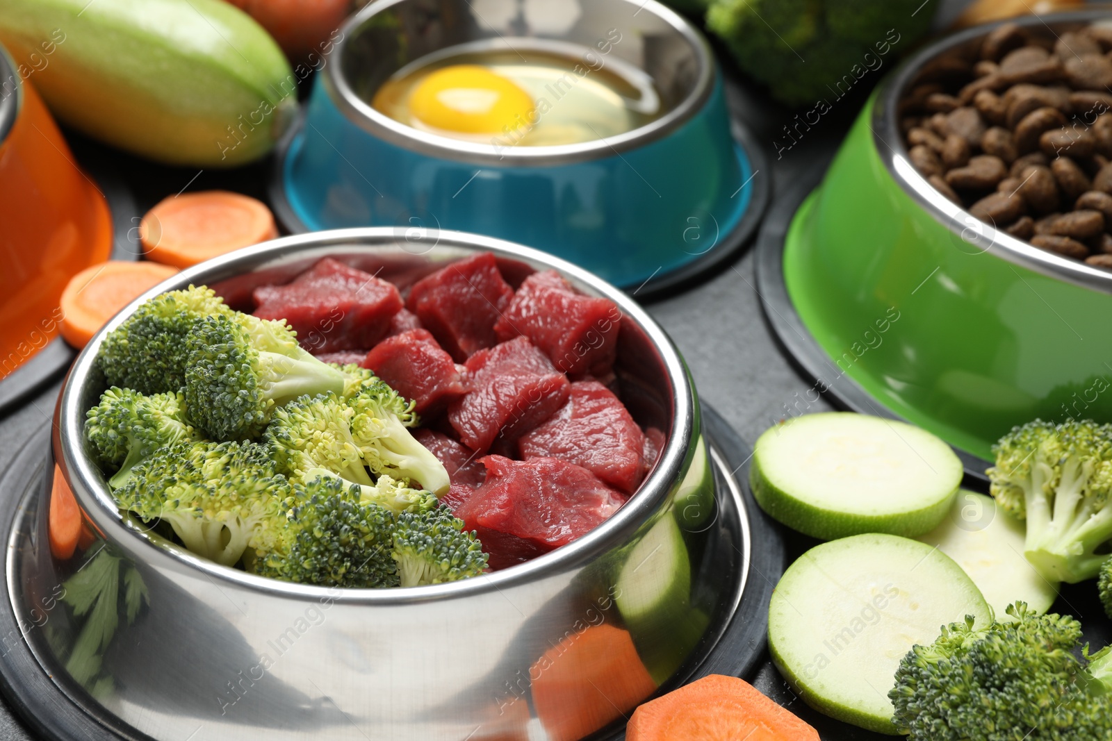 Photo of Natural and dry pet food in feeding bowls among products on grey table, closeup