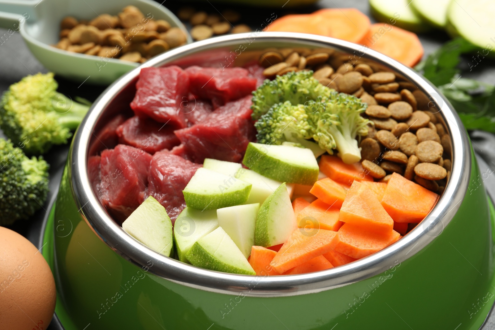 Photo of Natural and dry pet food in feeding bowl among products on table, closeup