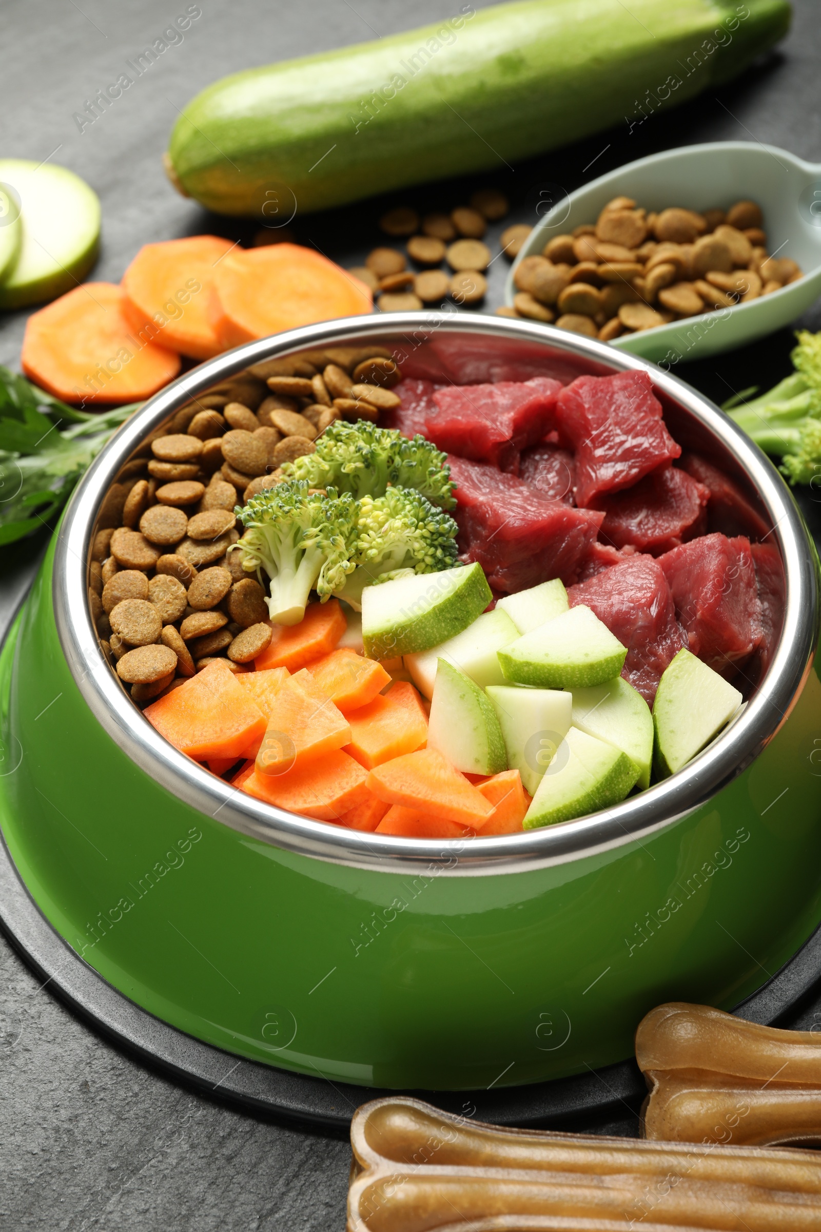 Photo of Natural and dry pet food in feeding bowl among products on dark textured table, closeup