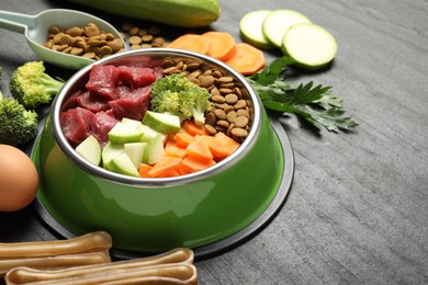 Photo of Natural and dry pet food in feeding bowl among products on dark textured table, closeup. Space for text