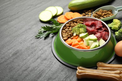 Photo of Natural and dry pet food in feeding bowl among products on dark textured table, closeup. Space for text