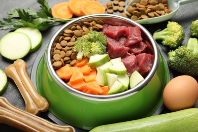 Photo of Natural and dry pet food in feeding bowl among products on dark table, closeup