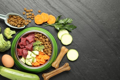 Photo of Natural and dry pet food in feeding bowl among products on dark textured table, flat lay. Space for text