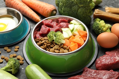 Photo of Natural and dry pet food in feeding bowls among products on dark table, closeup