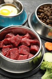 Photo of Natural and dry pet food in feeding bowls on dark table, closeup